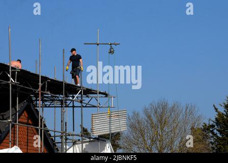 Zwei Männer, die Wellblech von der provisorischen Dachabdeckung des Neubaus entfernen Stockfoto