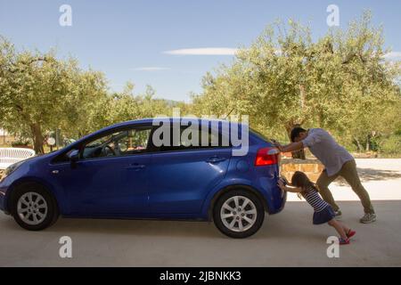 Bild eines Mannes, der mit seiner Tochter ihr Auto schiebt, nachdem er eine Panne hatte und das Benzin ausging. Verweis auf den aktuell teuren Kraftstoff Stockfoto