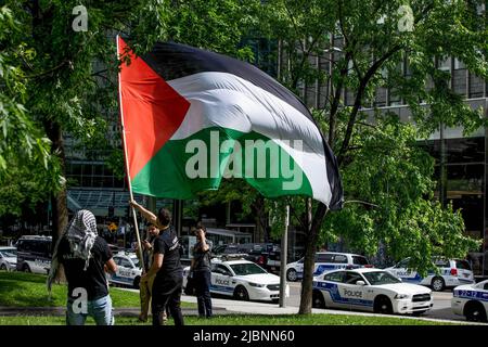 Ein Demonstranten sah während des Protestes die palästinensische Flagge vor Dutzenden von SPVM-Fahrzeugen schwenken. Hunderte versammelten sich auf dem Dorchester-Platz, um gegen die israelische Besatzung Palästinas zu protestieren, Fahnen zu schwenken und Gerechtigkeit für den ermordeten Al-Jazeera-Journalisten Shireen Abu Akneh, die Angriffe während ihres Begräbnisses, die Gewalt in Al Aqsa in Jerusalem und die Vertreibung palästinensischer Familien aus dem Sheikh-Jarrah-Viertel zu fordern. Die Demonstranten riefen „steht mit den Palästinensern in Jerusalem“, „Jerusalem gehört den Palästinensern“, „Wir sind Al Aqsa“ und „Wir werden euch nie sterben lassen“ und sprachen sich gegen den wachsenden Konflikt aus Stockfoto