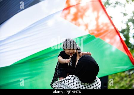 Eine Mutter hält ihr Baby während des Protestes vor die palästinensische Flagge. Hunderte versammelten sich auf dem Dorchester-Platz, um gegen die israelische Besatzung Palästinas zu protestieren, Fahnen zu schwenken und Gerechtigkeit für den ermordeten Al-Jazeera-Journalisten Shireen Abu Akneh, die Angriffe während ihres Begräbnisses, die Gewalt in Al Aqsa in Jerusalem und die Vertreibung palästinensischer Familien aus dem Sheikh-Jarrah-Viertel zu fordern. Die Demonstranten riefen „steht mit den Palästinensern in Jerusalem“, „Jerusalem gehört den Palästinensern“, „Wir sind Al Aqsa“ und „Wir werden euch nie sterben lassen“ und sprachen sich gegen die wachsenden Konflikte zwischen Israel und Ham aus Stockfoto