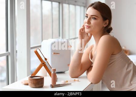 Schöne junge Frau mit kleinem Kühlschrank für Kosmetika zu Hause Stockfoto