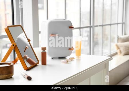 Kleiner Kühlschrank für Kosmetikprodukte und Spiegel auf dem Tisch Stockfoto