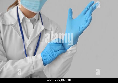 Ärztin setzt Gummihandschuhe vor grauem Hintergrund an Stockfoto