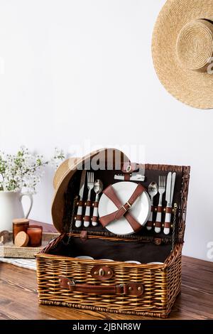 Korbkorb mit Geschirr für Picknick auf dem Tisch in der Nähe der Lichtwand Stockfoto