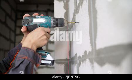 Close-up, die Hand eines Arbeiters mit einem Schraubendreher, verdreht die Schraube in die Wand. Er bohrt Bit knallen in Nahaufnahme in die Betonwand des Raumes. Stockfoto