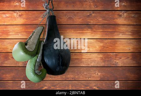 Alte Boxhandschuhe und Boxsack hängen auf Holzhintergrund Stockfoto