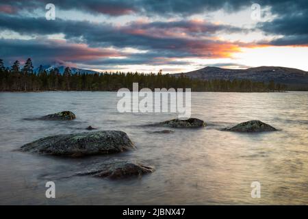 Große Felsbrocken im Wasser und farbenprächtiger Himmel an einem Sommerabend am See Isteren in Engerdal, Norwegen, Skandinavien. Stockfoto