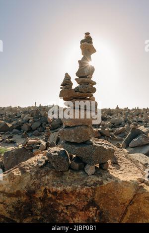 Pyramide aus Meereskieseln an einem sonnigen felsigen Strand bei Sonnenuntergang. Life Balance und Harmonie Konzept, vertikale Banner Stockfoto