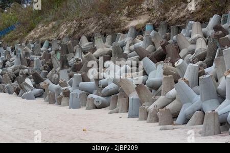 Betonbruchwässer aus Tetrapodenblöcken. Wellenbrecher am Strand und in den Dünen. Betonblöcke am Strand. Stockfoto