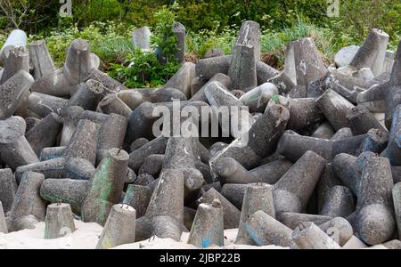 Betonbruchwässer aus Tetrapodenblöcken. Wellenbrecher am Strand und in den Dünen. Betonblöcke am Strand. Stockfoto