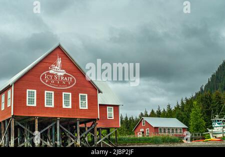 Hoonah, Alaska, USA - 18. Juli 2011: Red Ice Strait Point Gebäude mit Emblem am Tiefwasserhafen unter grauer Wolkenlandschaft. Grüner Wald im Rücken und U Stockfoto