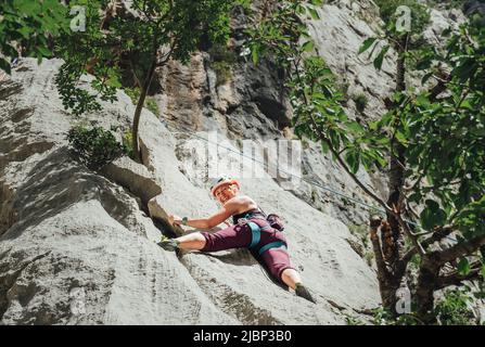 Lächelnde athletische Frau in Schutzhelm Klettern Klippe Felswand mit Top-Seil und Klettergurt in Paklenica Nationalpark-Website in Kroatien. A Stockfoto