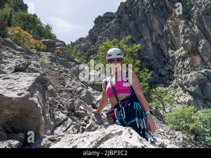 Fröhliche lächelnde Alpinistin Frau im schützenden Helm Klettergurt mit Schnellzuchten in Paklenica Nationalpark Schlucht in Kroatien. Aktive extreme spo Stockfoto