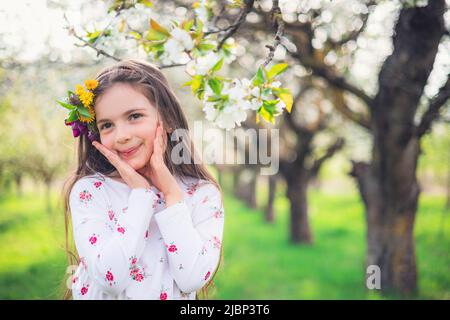 Glückliches schönes Mädchen genießen blühende Frühlingsbäume in Apfelgarten. Bulgarische Frau in Folklore-Kleid auf dem Feld. Stockfoto