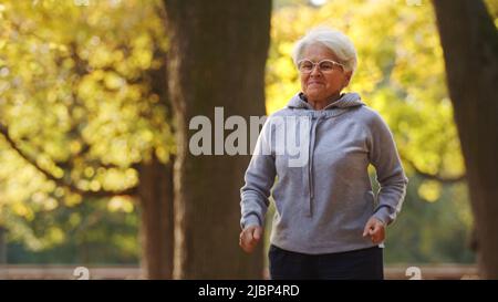 Senior grauhaarige Frau läuft Sprünge Park Hintergrund Medium Schuss Kopie Raum . Hochwertige Fotos Stockfoto