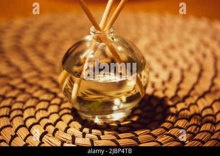 Diffusoria auf Rattan Hintergrund. Glasflasche mit Duftstäbchen. Duftzubehör, Wohnkultur. Aroma Duft Reed difusser. Aromatheropy-Konzept. Stockfoto