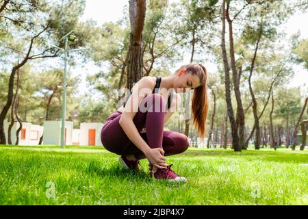 Junge Brünette Frau trägt sportliche Kleidung im Stadtpark, im Freien leiden an einer Knöchelverletzung beim Training und Laufen. Gesundheit und Sport Stockfoto