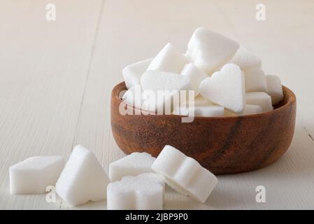 Brückenförmige Zuckerwürfel in Holzschüssel auf weißem Holzhintergrund. Nahaufnahme aus dem unteren Winkel, keine Personen. Stockfoto