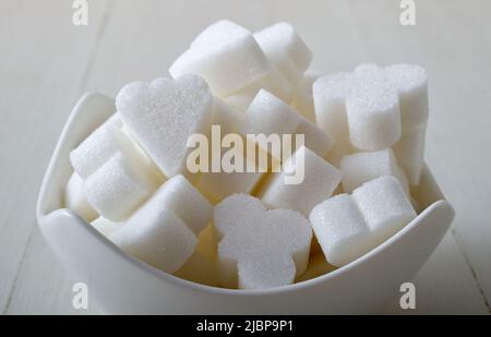 Brückenförmige Zuckerwürfel in einer Porzellanschale auf weißem Holzhintergrund. Nahaufnahme aus dem unteren Winkel, keine Personen. Stockfoto