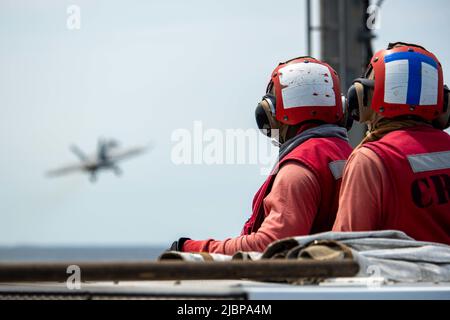 220607-N-DW158-2037 PAZIFISCHER OZEAN (7. Juni 2022) Airman Moussa Doumbia, links, aus New York, Und Joshua Hugget, Fluggast von Aviation Boatswain, aus Fontana, Kalifornien, beobachtet eine F/A-18E Super Hornet, die an das Royal Maces of Strike Fighter Squadron (VFA) 27 angeschlossen ist und vom Flugdeck des einzigen vorwärts eingesetzten Flugzeugträgers der US Navy USS Ronald Reagan (CVN 76) gestartet wird. Die Royal Maces führen Luftangriff- und Streikkräfte-Escort-Missionen sowie Schiffe, Kampfgruppen- und Geheimdiensteintreibemissionen durch. Ronald Reagan, das Flaggschiff der Carrier Strike Group 5, pro Stockfoto