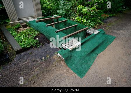 Öffnen Sie frisch ausgegrabenes Grab mit grüner Abdeckung auf einem alten kölner Friedhof Stockfoto