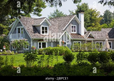 Neues Haus im Hampton Cottage-Stil, eingerahmt von Sträuchern und Pinus - Kiefernästen im Frühling. Stockfoto