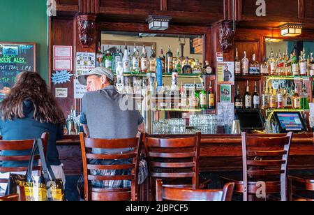 Skagway, Alaska, USA - 20. Juli 2011: Blick auf Menschen, die an einer braunen Holzbar in der Skagway Brewing Company sitzen. Wasserhähne, Glaswaren und viele harte Stockfoto