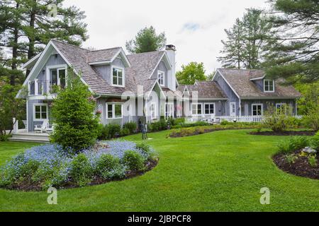 Neues Hampton-Haus mit landschaftlich gestaltetem Vorgarten und blauem Myosotis - Vergissmeinnicht-Blumen an der Grenze im Sommer. Stockfoto