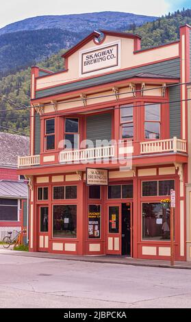 Skagway, Alaska, USA - 20. Juli 2011: Rot, grün und gelb Skagway Brewing Company Fassade am Broadway grün bewaldeten Berg im Rücken. Stockfoto