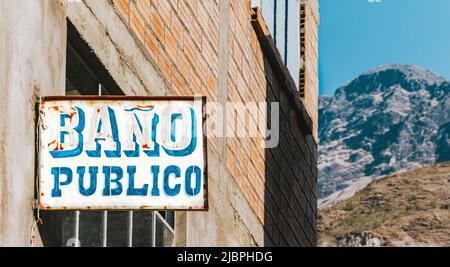 QUIME, LA PAZ, BOLIVIEN - 30. JULI 2016: Ein rustikales öffentliches Toilettenschild mit Berg im Hintergrund in Quime, Bolivien. Quime ist eine kleine Stadt Stockfoto