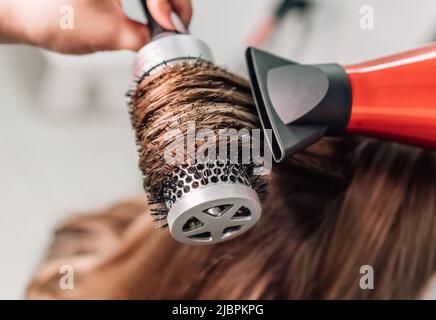 Trocknen lange braune Haare mit einem Fön und einer runden Bürste. Schließen. Hochwertige Fotos Stockfoto