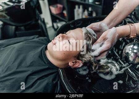 Frau, die Shampoo anwendet und die Haare des Kunden massiert. Eine Frau, die sich beim Friseur die Haare wäscht. Hochwertige Fotos Stockfoto