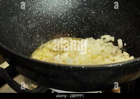 Fein gehackte Zwiebeln werden in Öl in einer Pfanne auf dem Gasherd gebraten Stockfoto