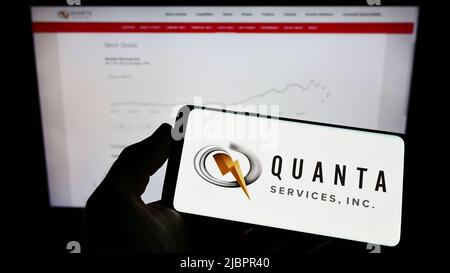 Person mit Mobiltelefon und Logo des US-Infrastrukturunternehmens Quanta Services Inc. Auf dem Bildschirm vor der Webseite. Konzentrieren Sie sich auf die Telefonanzeige. Stockfoto