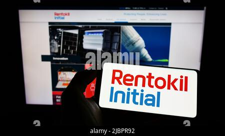 Person, die das Smartphone mit dem Logo des britischen Dienstleistungsunternehmens Rentokil Initial plc auf dem Bildschirm vor der Website hält. Konzentrieren Sie sich auf die Telefonanzeige. Stockfoto