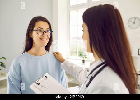 Frau an der Rezeption bei einer fürsorglichen Ärztin, die ihre Hand in der Arztpraxis auf die Schulter des Patienten legt Stockfoto