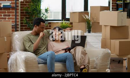 Diverse paar Surfen im Internet, um Dekor auf Laptop kaufen, Kauf von Wohnmöbeln auf Online-Shopping, um Wohnzimmer Wohnung zu schmücken. Umzug in gemieteten Haushaltsimmobilien zusammen. Stativaufnahme. Stockfoto