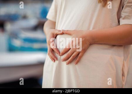 Nicht erkennbare Schwangere lächelt, schaut auf den Bauch, berührt den Bauch, kümmert sich um zukünftiges Baby im Bauch. Hafen, Hafen Stockfoto