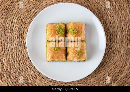 Pistazien Baklava auf einem weißen Teller. Eine Baklava-Platte auf einem Korbhintergrund Stockfoto