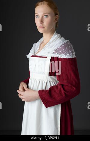 Ein Regency Dienstmädchen, das ein rotes Kleid und eine Schürze trägt Stockfoto