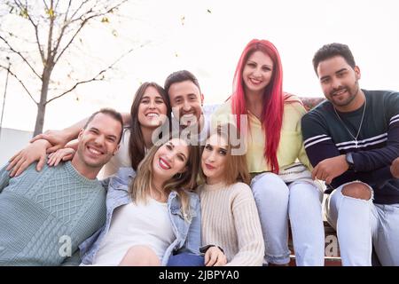 Eine Gruppe von Freunden lächelt der Kamera zu, während sie zusammen auf einer Bank sitzen. Konzept von Freundschaft und Positivität. Stockfoto