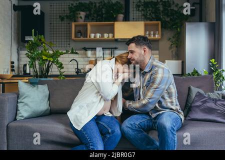 Schwanger Frau zu Hause sitzt auf dem Sofa traurig und weinend, Ehemann beruhigt und unterstützt, junges Ehepaar Stockfoto