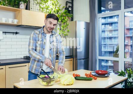 Der Mann bereitet zu Hause gesunde und gesunde Lebensmittel zu, schneidet Gemüse für Salat in der Küche Stockfoto