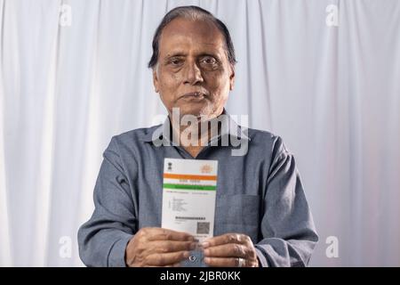 Ein alter indischer Mann, der mit einer Aadhaar-Karte in den Händen auf weißem Hintergrund lächelt Stockfoto