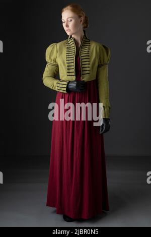 Regency-Frau mit spencer aus grünem Leinen und rotem Kleid vor Studiokulisse Stockfoto