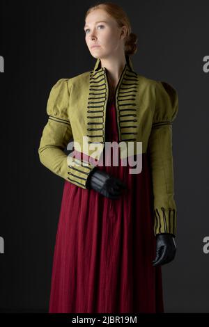 Regency-Frau mit spencer aus grünem Leinen und rotem Kleid vor Studiokulisse Stockfoto