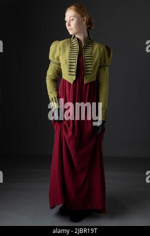 Regency-Frau mit spencer aus grünem Leinen und rotem Kleid vor Studiokulisse Stockfoto