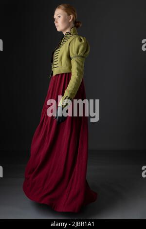 Regency-Frau mit spencer aus grünem Leinen und rotem Kleid vor Studiokulisse Stockfoto