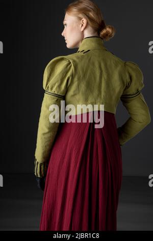 Regency-Frau mit spencer aus grünem Leinen und rotem Kleid vor Studiokulisse Stockfoto