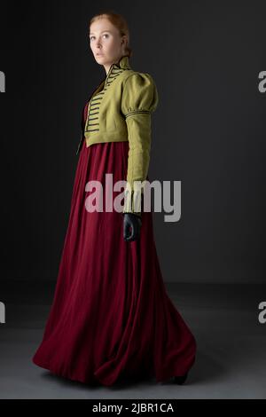 Regency-Frau mit spencer aus grünem Leinen und rotem Kleid vor Studiokulisse Stockfoto